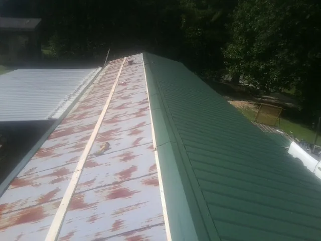 Old rusted panels beside newly installed green metal roofing — Wind Damage Roof Repair by Roofing Brothers in Reedsville
