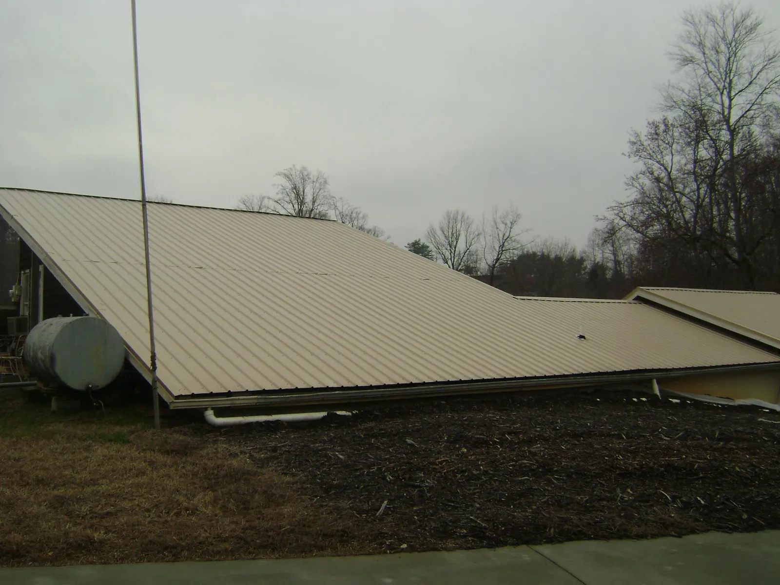 Wide tan metal roof plane seen from the ground beside a propane tank in Reedsville